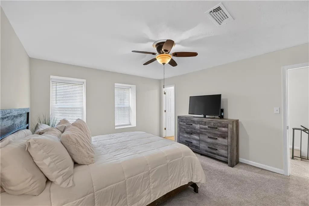 Neutral-toned interior featuring wall-to-wall carpeting, dual windows with integrated blinds, and a central ceiling fan with integrated light fixture