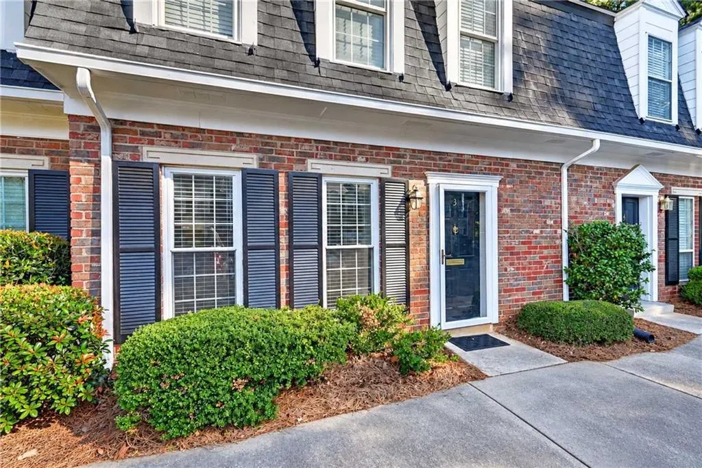 Brick exterior featuring a mansard roofline, multi-pane windows with decorative shutters, and individual entry doors