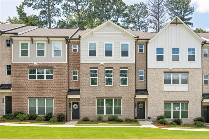 Brick and siding exterior with gabled accents, multiple windows, dark entry doors, and a manicured lawn