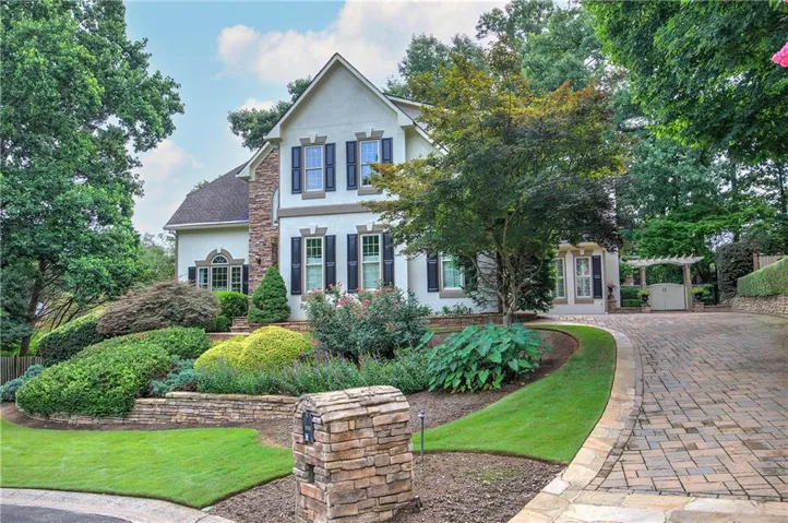 Stucco exterior featuring stone accents, dark shutters, a gabled roof, stone driveway, and a stone mailbox