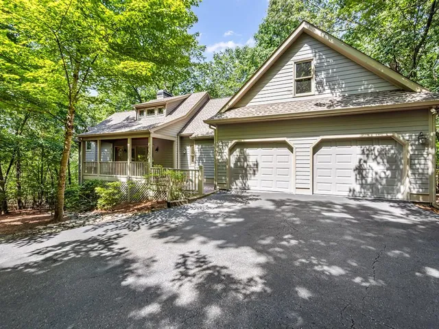 Gable roofline residence featuring light-colored siding, an attached two-car garage with panel doors, a covered porch with a wood railing, multiple dormer windows, and a paved driveway