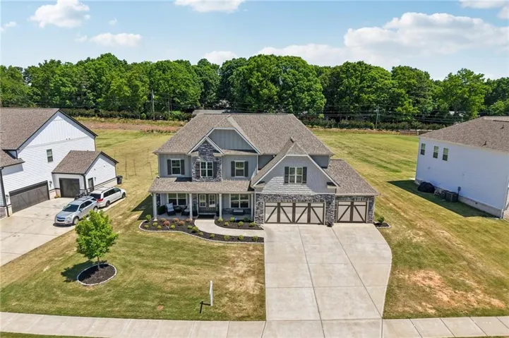 Two-story residence featuring a covered front porch, stone and siding exterior, a three-car garage with carriage-style doors, and a concrete driveway