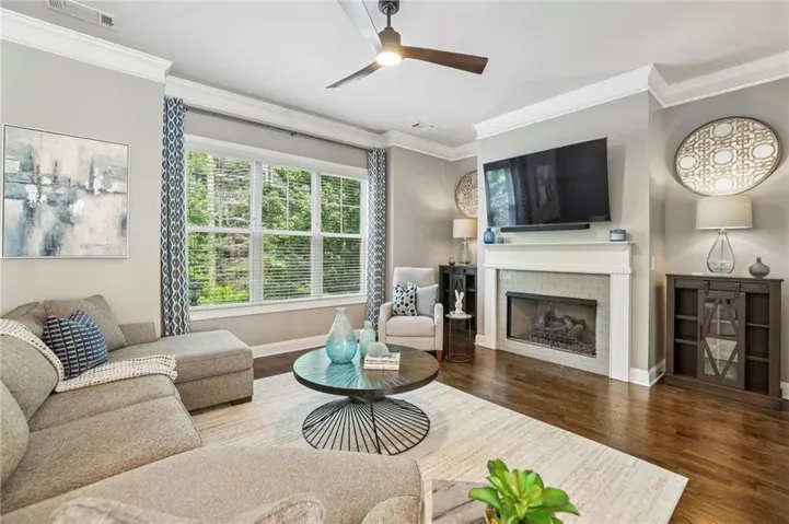 Living area featuring dark wood-finish flooring, a contemporary ceiling fan, and a fireplace with a light tiled surround and white mantel