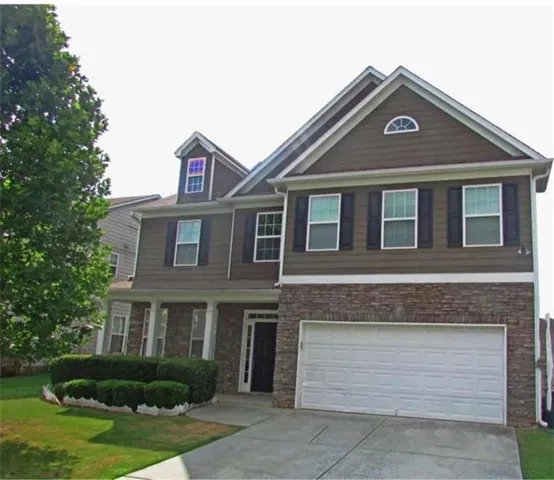 Two-story exterior with siding and stone accents, featuring a two-car garage, covered porch with columns, and dormer windows