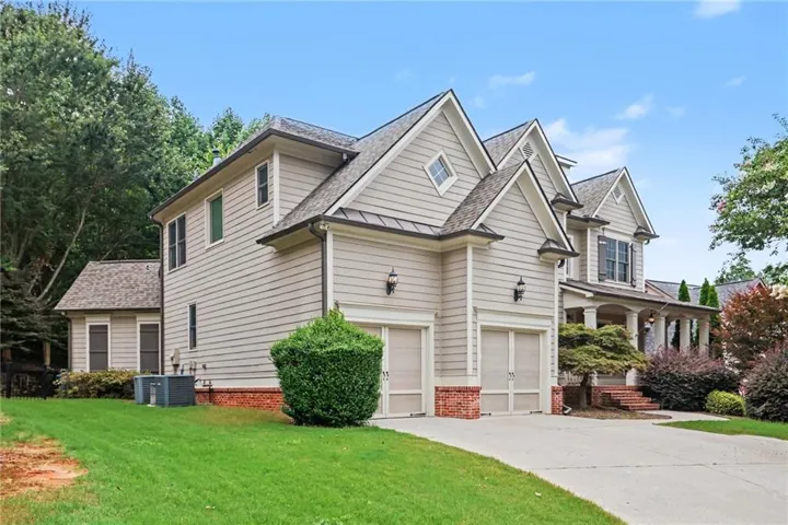 Light-colored horizontal siding exterior featuring multiple gables, a two-car garage with brick accents, a covered porch, and mature landscaping