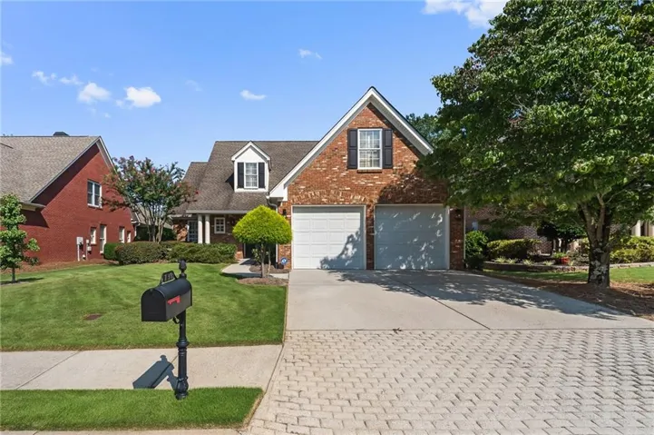 Brick exterior with dormer windows, attached two-car garage, concrete driveway, and paver stone parking pad