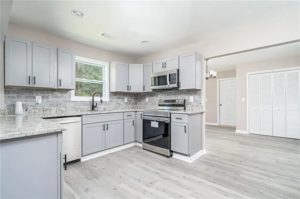 Kitchen with stainless steel appliances, gray cabinets, backsplash, light wood-style floors, and light stone counters