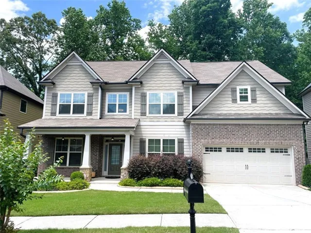 Two-story residence featuring a brick and siding exterior, an attached two-car garage, and a covered front porch