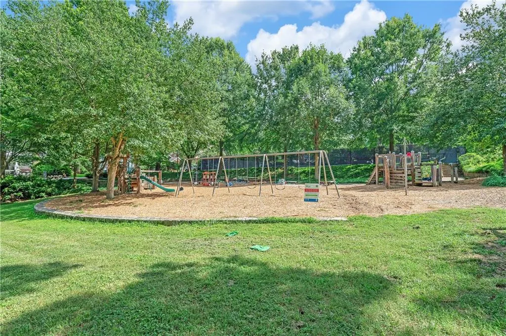 Expansive green space featuring a dedicated play area, swing sets, a wooden play structure with slides, and mature shade trees