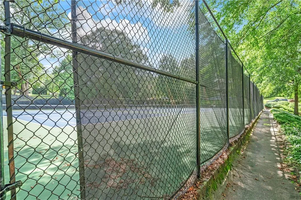 Outdoor tennis court with a chain-link fence and surrounding pathways