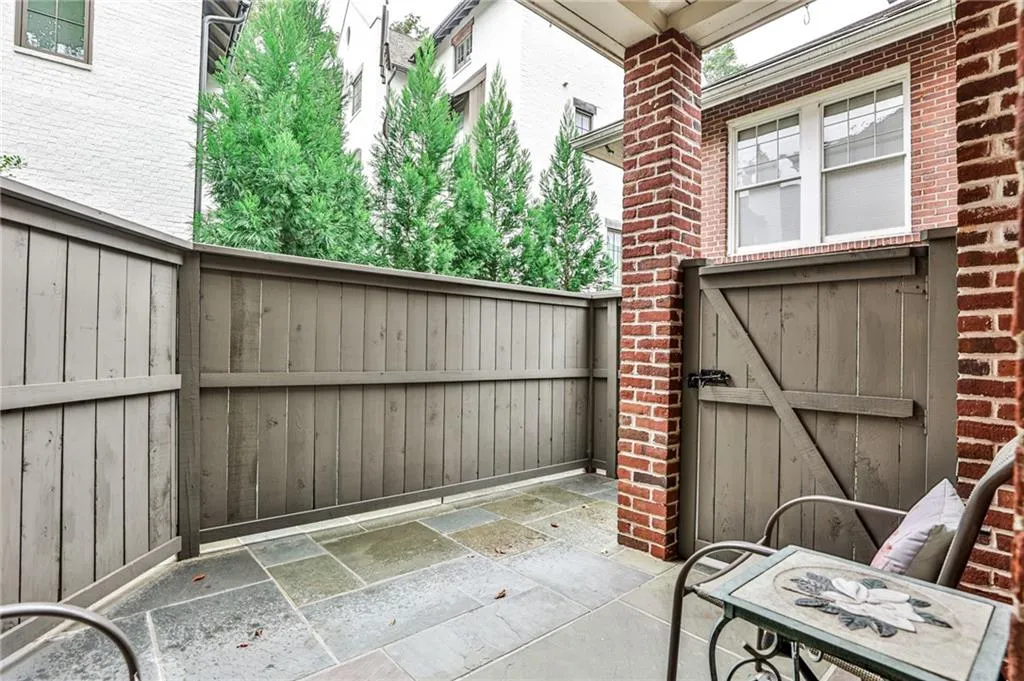 Paved patio with large format stone tiles, enclosed by a privacy fence, and featuring a brick column