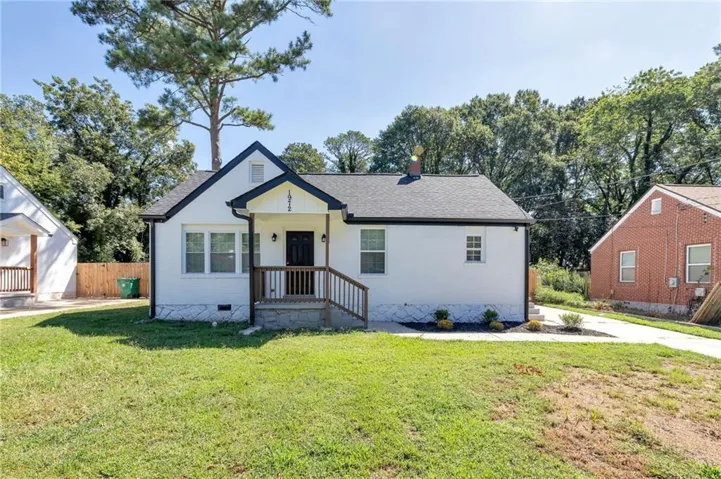 White exterior with dark trim accents, a covered front porch featuring wood railings, and a dark entry door