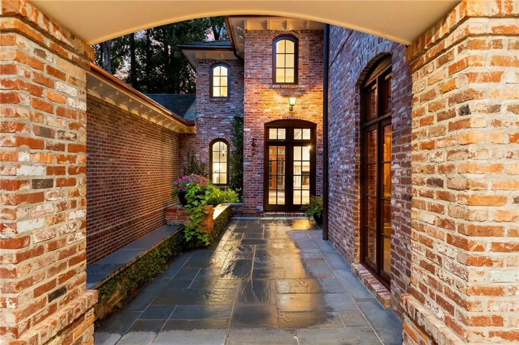 Brick exterior with arched entryway, stone walkway, dark-framed windows, and a double-door entry