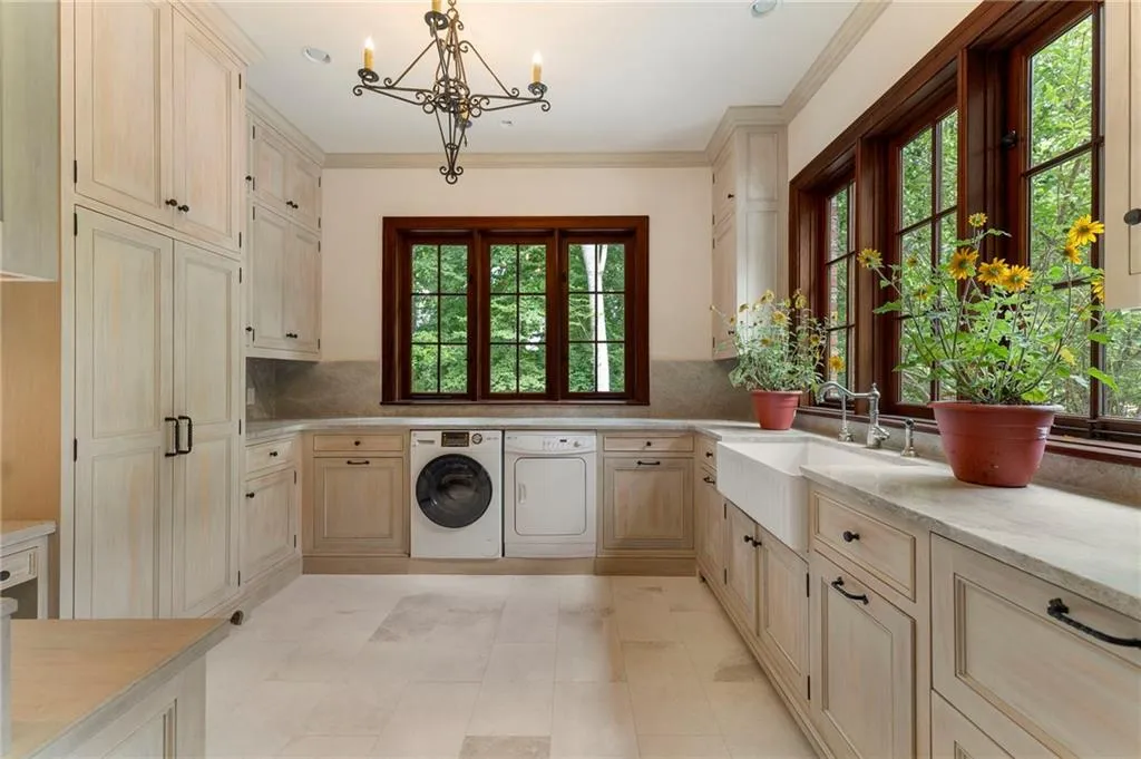 Expansive laundry room featuring abundant light-toned cabinetry, a built-in farmhouse sink, and large casement windows with dark wood trim