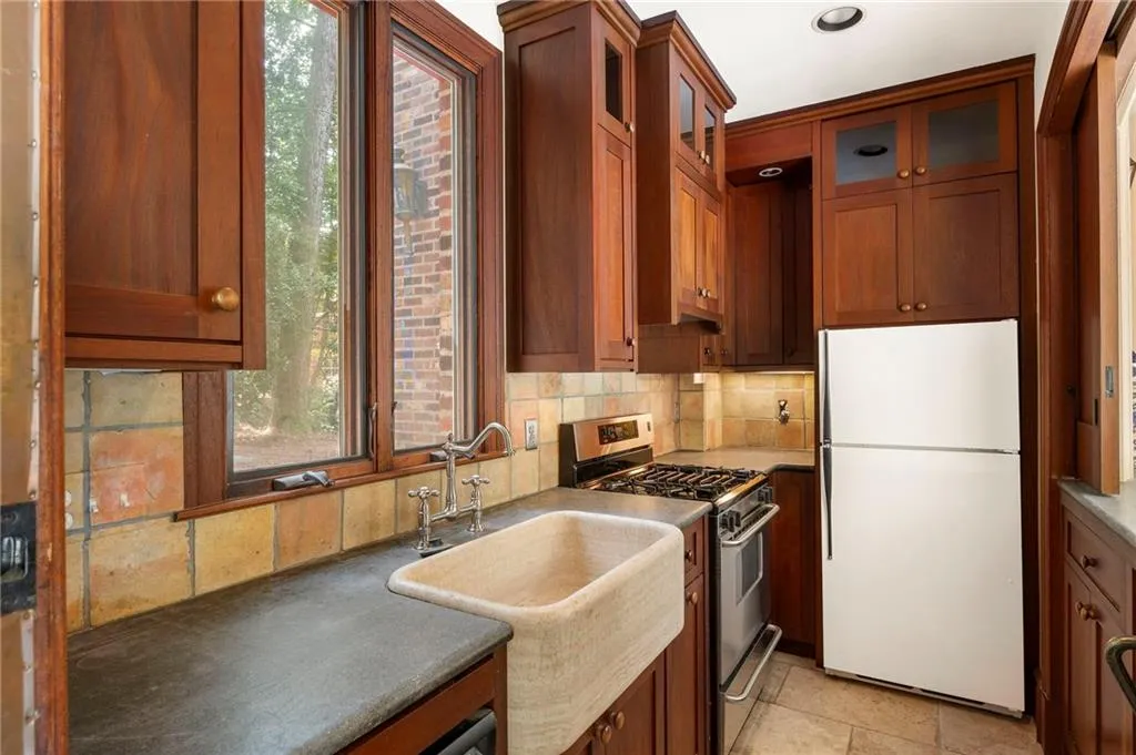 Kitchen featuring rich wood cabinetry, a farmhouse-style sink, stone countertops, and tile backsplash