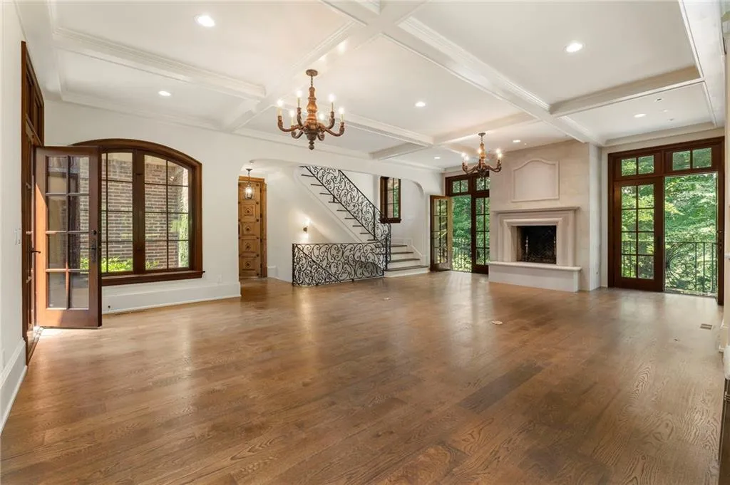 Spacious room featuring wood-finish flooring, a coffered ceiling, and a prominent fireplace with a stone mantel