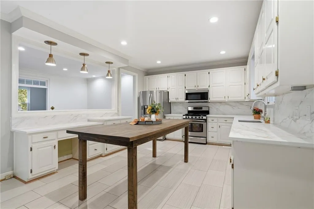 Kitchen with backsplash, appliances with stainless steel finishes, crown molding, white cabinets, and light stone countertops