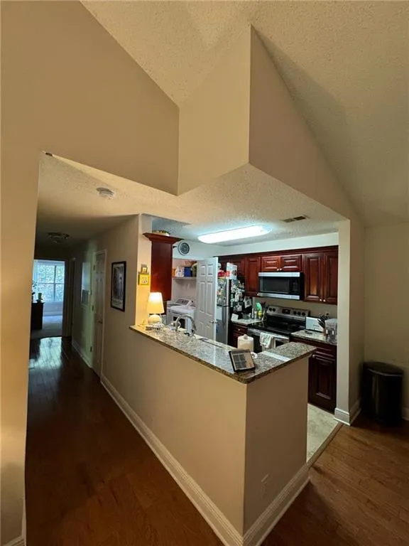 Kitchen featuring kitchen peninsula, hardwood / wood-style flooring, stainless steel appliances, and a textured ceiling