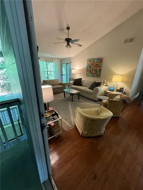 Living room featuring wood-type flooring, ceiling fan, vaulted ceiling, and a textured ceiling