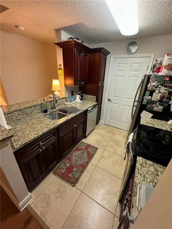 Kitchen featuring sink, light tile patterned flooring, kitchen peninsula, appliances with stainless steel finishes, and a textured ceiling