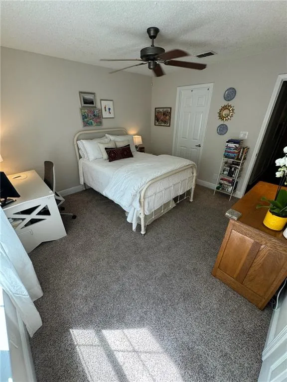 Bedroom featuring dark colored carpet, ceiling fan, a closet, and a textured ceiling