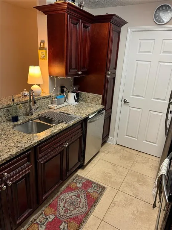 Kitchen featuring light tile patterned floors, sink, kitchen peninsula, stainless steel dishwasher, and light stone countertops