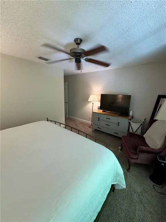 Carpeted bedroom with ceiling fan and a textured ceiling
