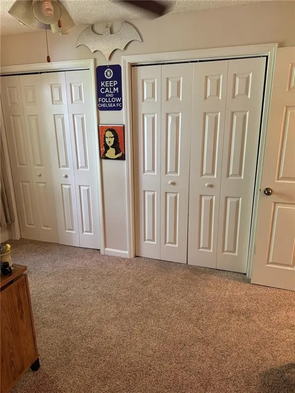 Unfurnished bedroom featuring ceiling fan, a textured ceiling, two closets, and carpet