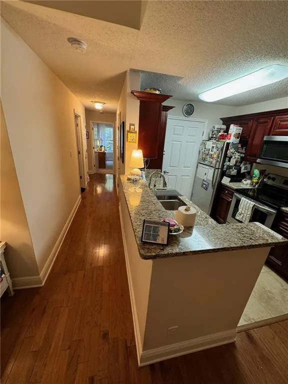 Kitchen with a textured ceiling, kitchen peninsula, stainless steel appliances, and dark hardwood / wood-style flooring