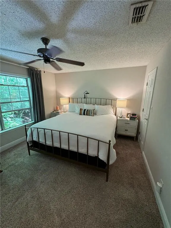 Carpeted bedroom featuring ceiling fan and a textured ceiling