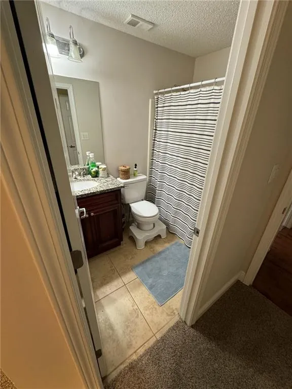 Bathroom with vanity, a textured ceiling, tile patterned floors, walk in shower, and toilet