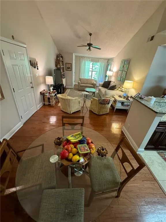 Living room with wood-type flooring, vaulted ceiling, a textured ceiling, and ceiling fan