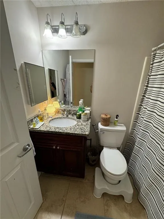 Bathroom featuring toilet, tile patterned floors, a shower with shower curtain, vanity, and a textured ceiling