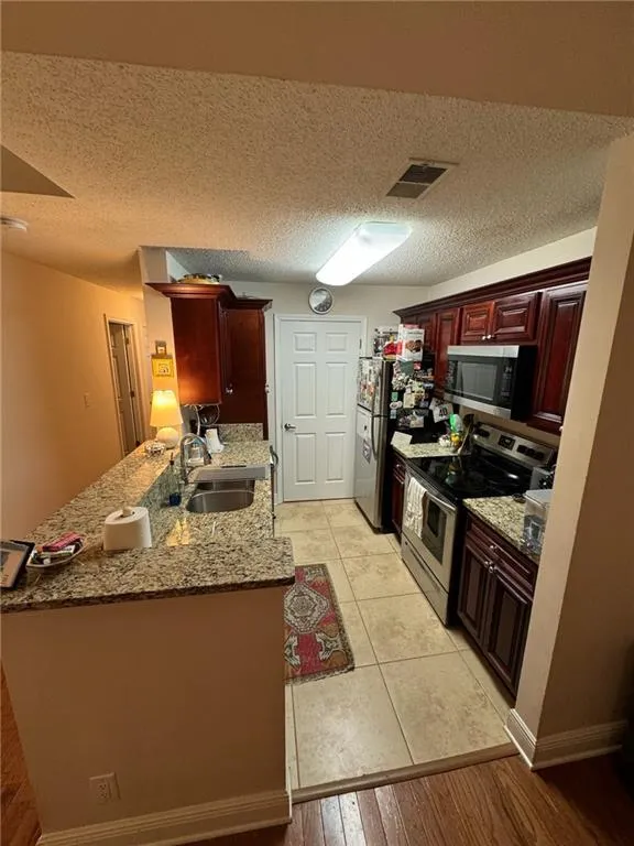 Kitchen with sink, kitchen peninsula, a textured ceiling, stainless steel appliances, and light wood-type flooring