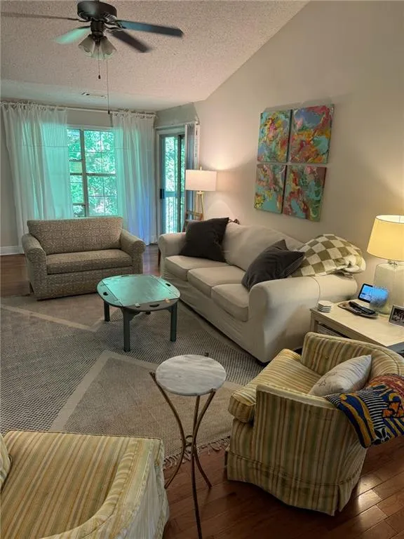 Living room with ceiling fan, a textured ceiling, lofted ceiling, and hardwood / wood-style floors