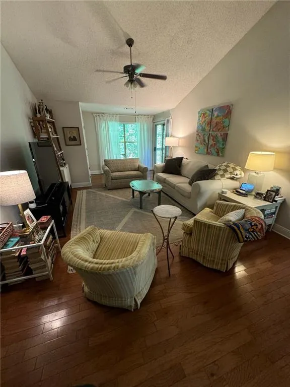 Living room with ceiling fan, dark hardwood / wood-style floors, vaulted ceiling, and a textured ceiling