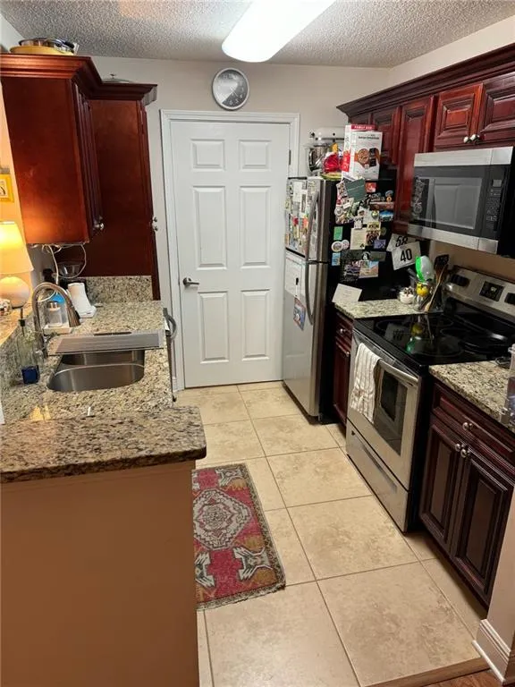Kitchen with light tile patterned flooring, sink, a textured ceiling, appliances with stainless steel finishes, and light stone countertops
