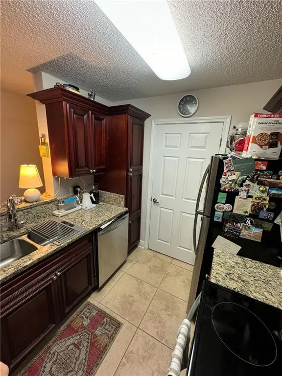 Kitchen with light tile patterned flooring, sink, stainless steel appliances, and a textured ceiling