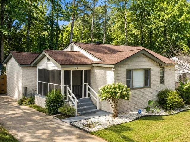 Ranch-style residence featuring a screened-in porch, light-colored brick exterior, and a brown shingled roof