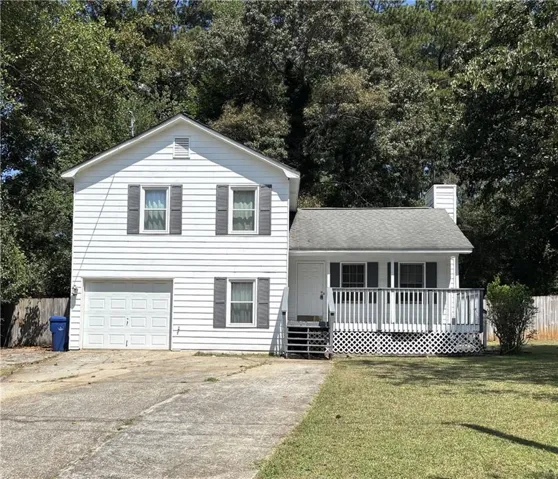 White-paneled exterior, attached garage, front porch with white railing, and a sloped driveway
