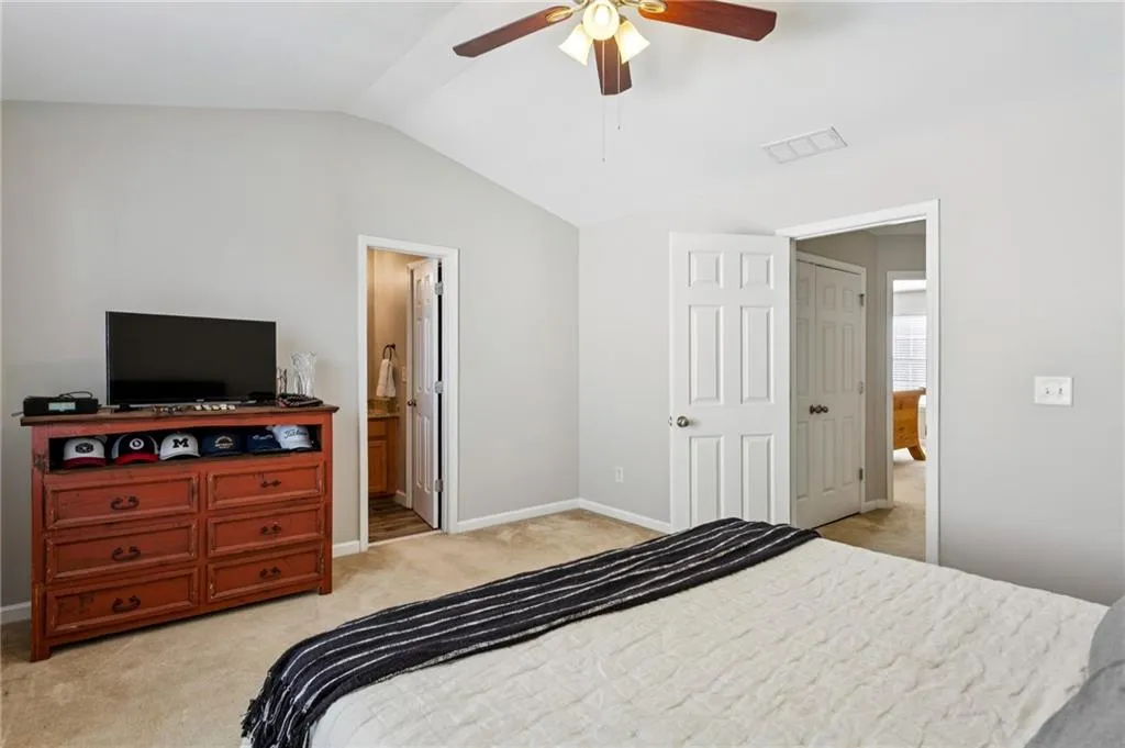 Bedroom featuring light carpet, lofted ceiling, a ceiling fan, and ensuite bathroom