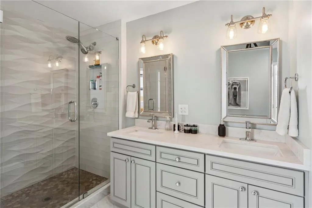 Bathroom with glass door shower, double vanity, and attractive lights and fixtures.