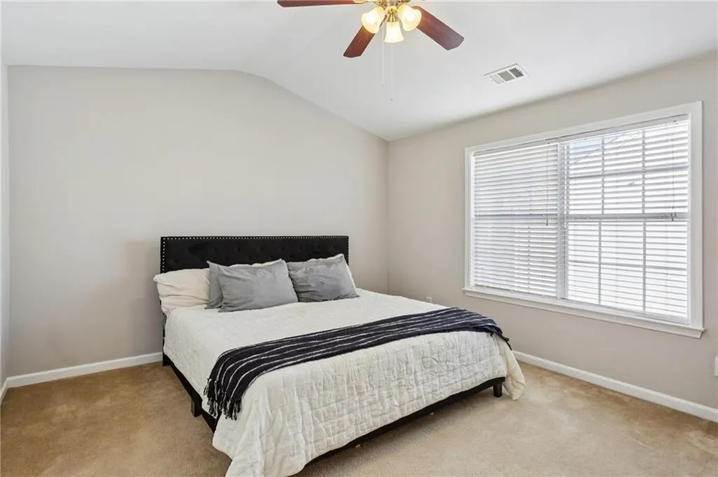 Carpeted bedroom featuring vaulted ceiling and a ceiling fan