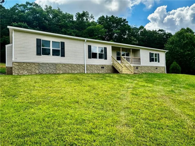 Horizontal vinyl siding, stone-finish foundation, covered front porch, wooden stairs with railings, and dark louvered shutters