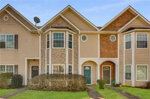 Townhome exterior featuring tan siding, brick accents, multiple gables, and individual entryways
