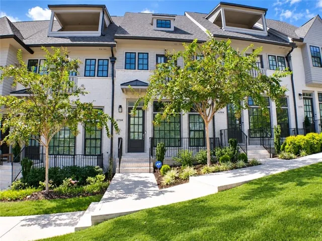 Modern townhome exterior featuring white brick, dark-framed windows, and a prominent dormer