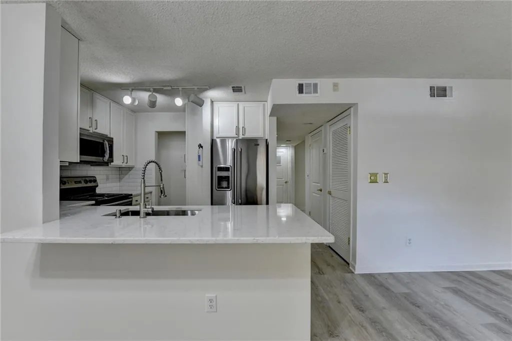 Kitchen featuring backsplash, appliances with stainless steel finishes, light stone counters, white cabinetry, and a textured ceiling