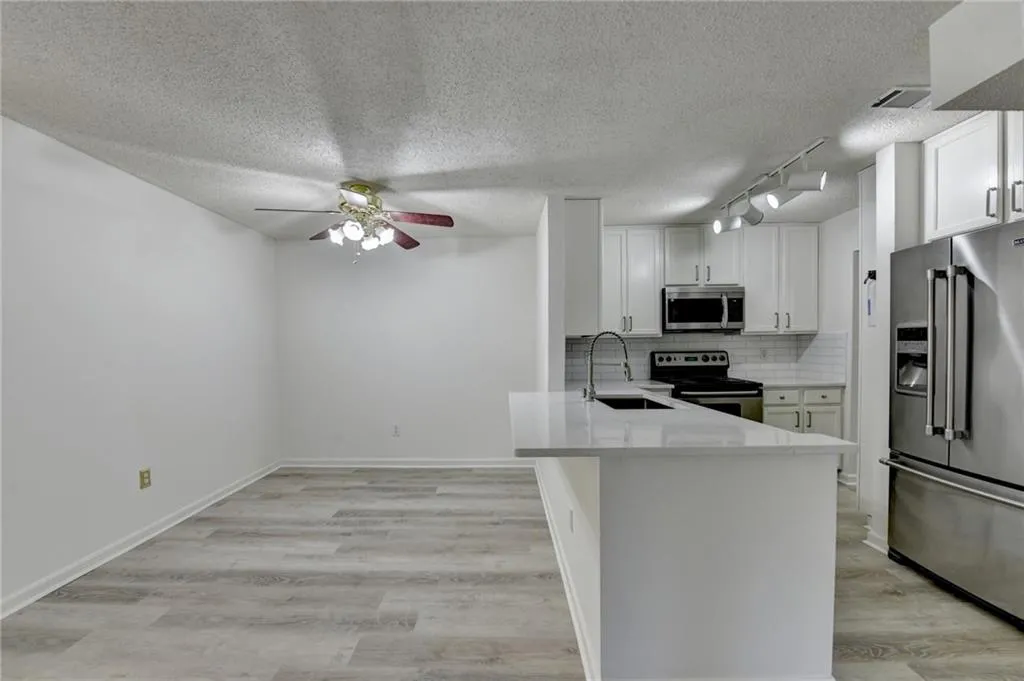 Kitchen featuring tasteful backsplash, stainless steel appliances, a textured ceiling, light stone countertops, and white cabinetry