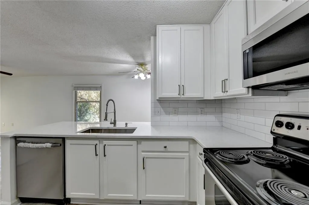 Kitchen featuring stainless steel appliances, decorative backsplash, a textured ceiling, white cabinetry, and light stone counters