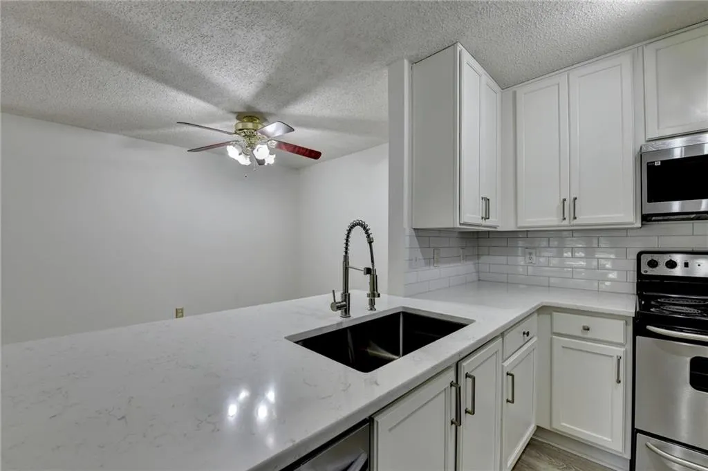 Kitchen with appliances with stainless steel finishes, decorative backsplash, white cabinetry, a textured ceiling, and light stone counters